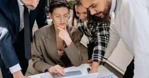 office team gathered around a laptop reviewing documents and digital notes