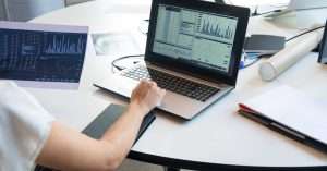 Person working at a laptop reviewing data charts and notes