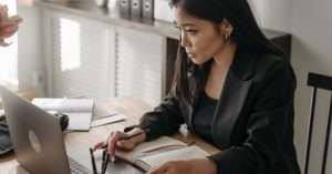 Adult working at a laptop with notes and a coffee in a home office, studying online