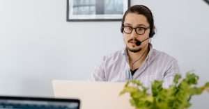 person wearing a headset using a laptop with a notebook and coffee on a tidy home office desk