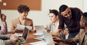 A team discussing project management tools around a table with laptops