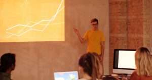 A professional presenting data on a laptop to an audience in an office setting