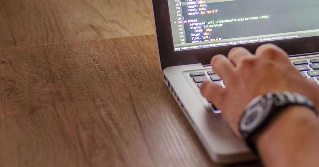 A young web developer focused on coding on a laptop in an office environment